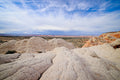 Rounded, cracked white sandstone stretching toward a wide desert horizon of striped mesas, wispy clouds sweeping overhead