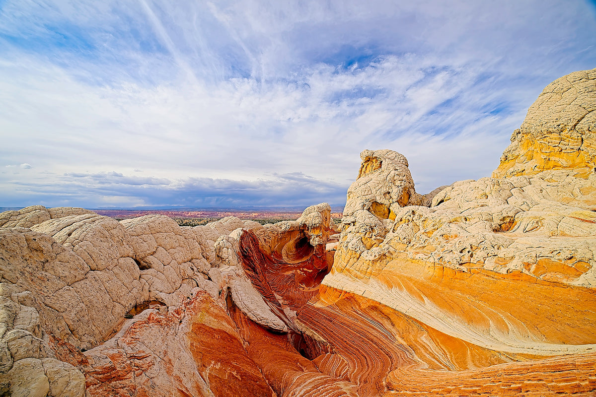Swirling vortex-like sandstone patterns of white and orange rock at White Pocket, wispy cirrus clouds streaking overhead