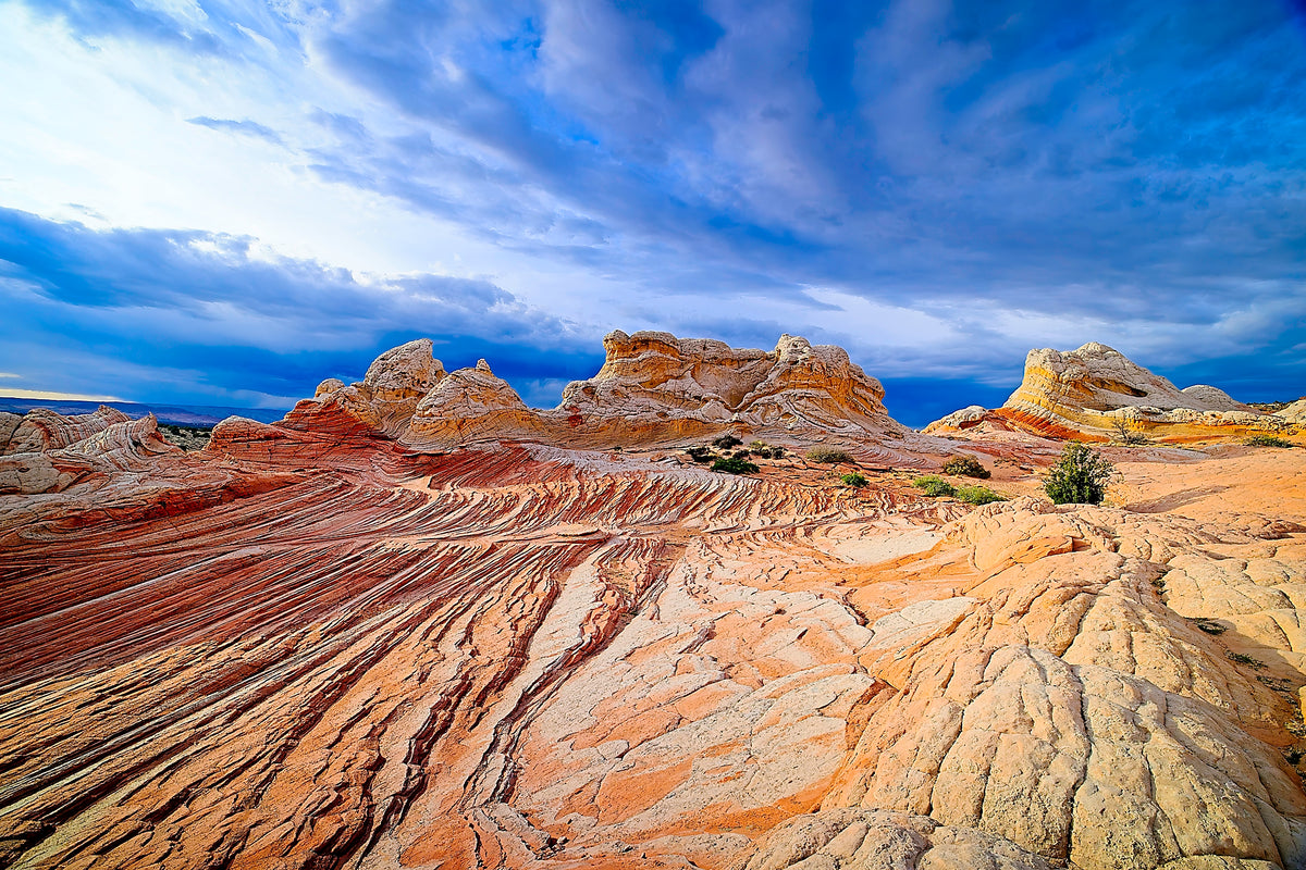 Rhythmic wavy striations of layered sandstone at White Pocket, dramatic clouds breaking with sunlight overhead