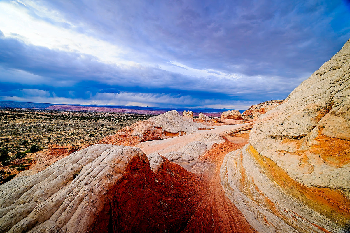 A winding channel of white and orange sandstone at White Pocket, a storm system building over the desert horizon beyond