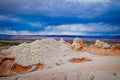Cracked white sandstone domes of White Pocket, streaks of rain falling from storm clouds over a distant red mesa