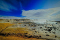 Steam rising from a geothermal field of mineral-crusted ochre and white ground, a sweeping cloud crossing a deep blue Icelandic sky