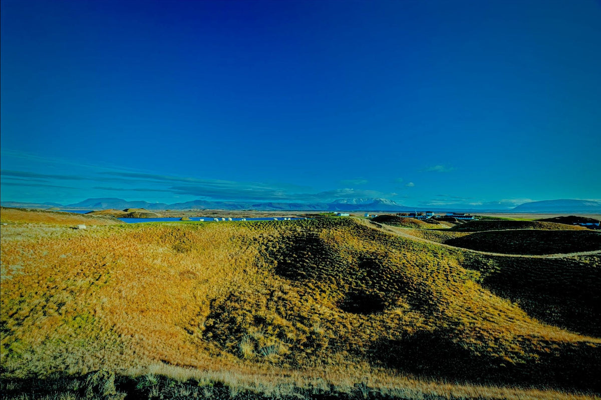 Rolling grass-covered pseudo-crater hills near Lake Myvatn, a distant lake and mountain range under a deep, clear blue sky