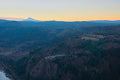 Mount Hood's distant peak catching last light beyond the forested Columbia River Gorge, a cliffside overlook road winding below at dusk