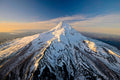The full symmetric snow-covered cone of Mount Hood catching golden sunlight, dark forested ridges falling away toward the horizon