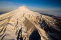 A dark rocky spine jutting from Mount Hood's snow-covered flank, clouds filling the valley beyond in morning light