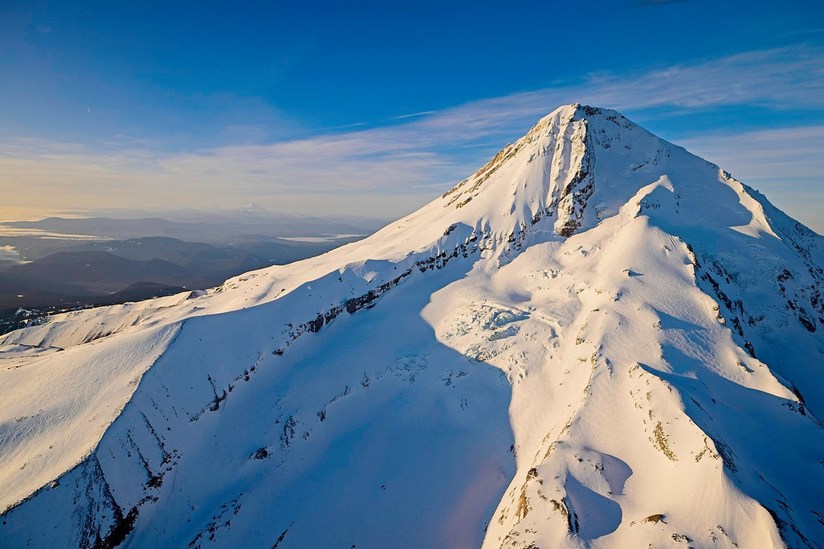 A knife-edge snow ridge on Mount Hood, deep shadow falling away on one side and sunlit snow on the other, hazy valley far below
