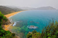 A golden sand beach curving along turquoise water, forested headlands fading into coastal haze