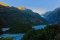 A braided glacial river winding through a forested valley toward the distant Franz Josef Glacier, a sunlit ridge catching the first light above