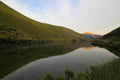 Grass-covered hills reflecting in the still water of Moke Lake, a distant peak catching the day's last sunlight