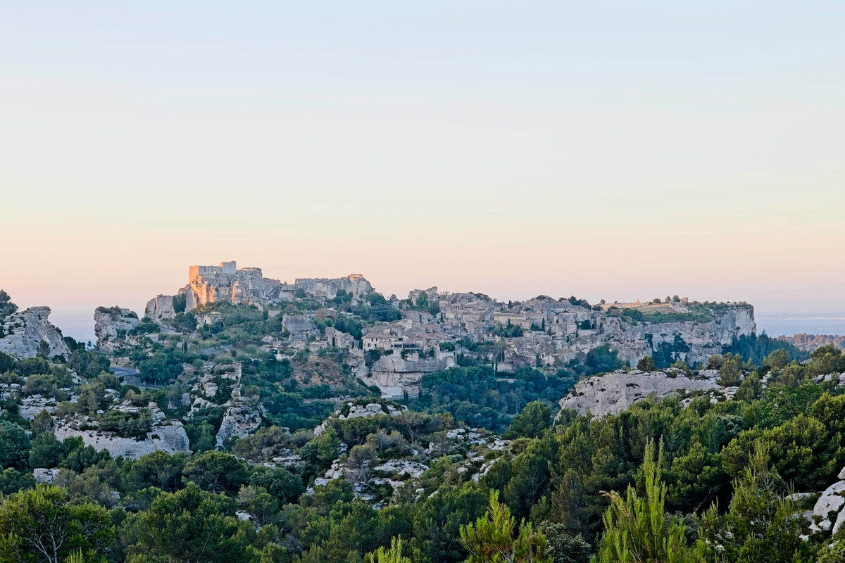 The citadel and village of Les Baux-de-Provence on its limestone ridge at dusk, pine and scrub filling the foreground, the last sun warm on the fortress wall