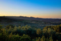 The Alpilles ridge in morning haze above a wide valley of olive groves and cultivated fields, deep blue sky over a warm horizon